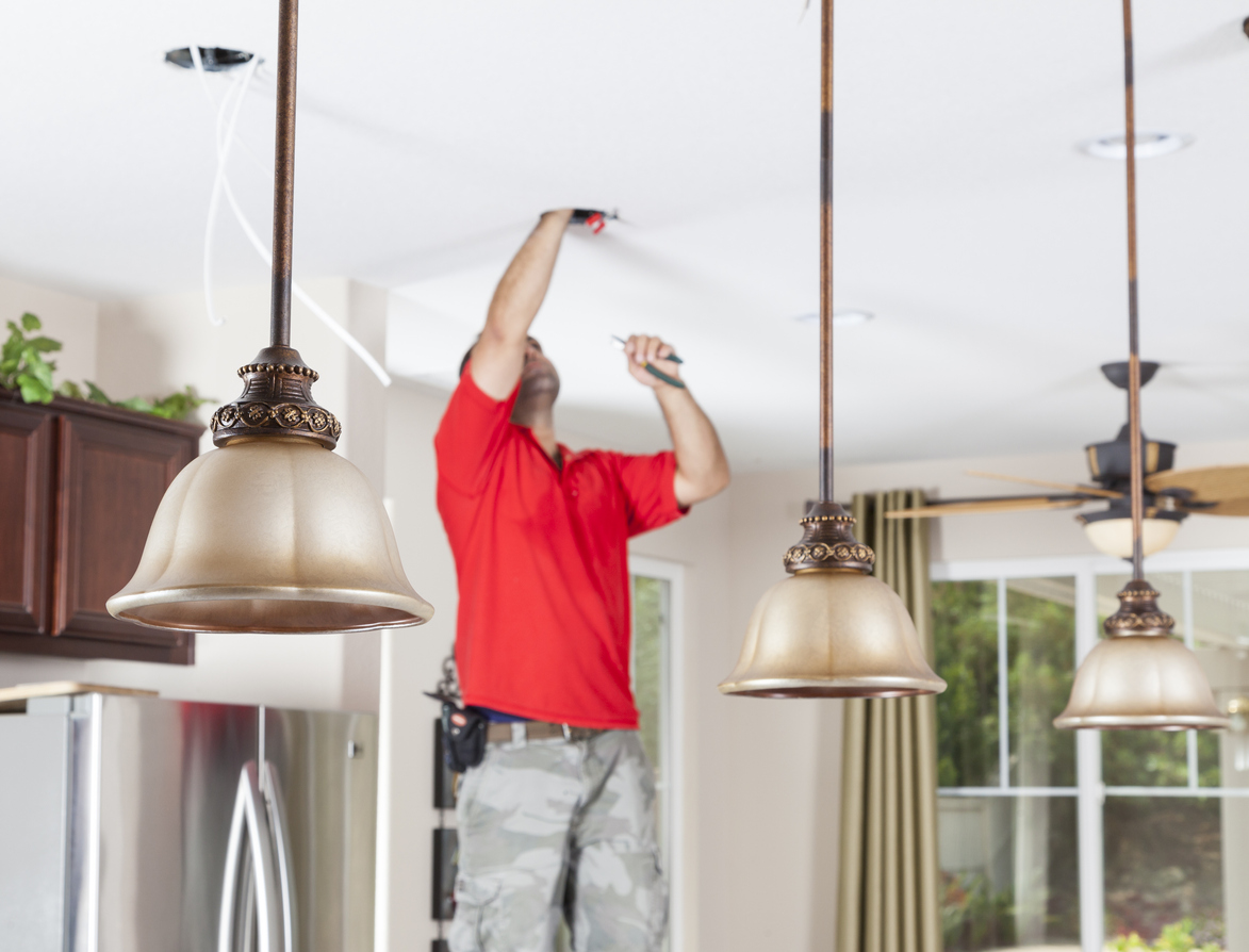 Man installing ceiling pendant lights and recessed lighting in kitchen